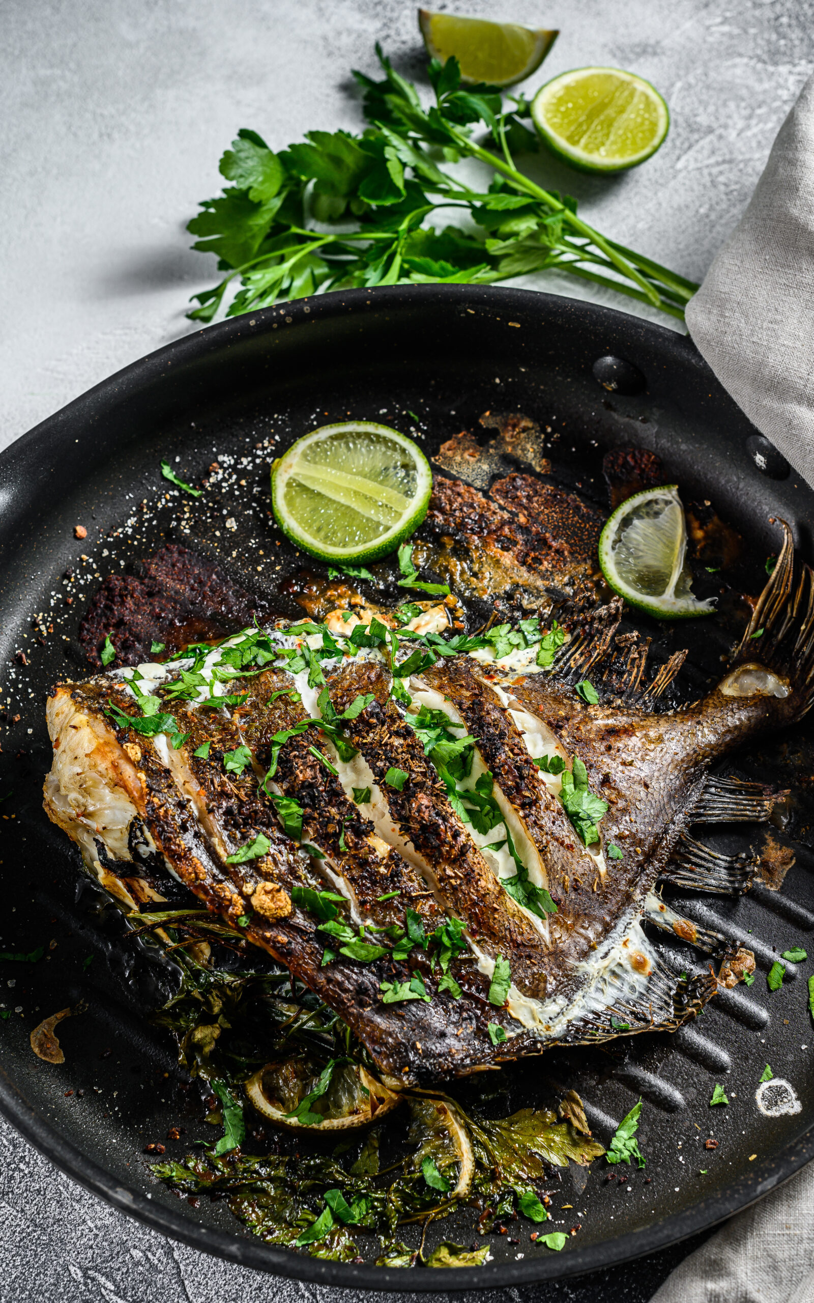 Grilled John Dory fish with lime and parsley in a pan. Gray background. Top view